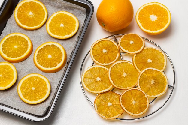 Rodajas de naranja secas en una parrilla de metal Rodajas de naranja frescas en una bandeja para hornear