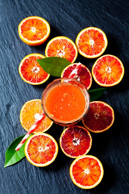 Rodajas de naranjas sanguinas y vaso de jugo de naranja en pizarra