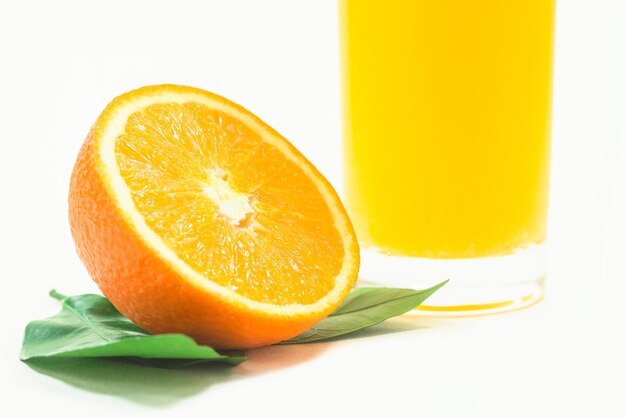 Rodajas de naranjas con un vaso de jugo de naranja sobre un fondo blanco.