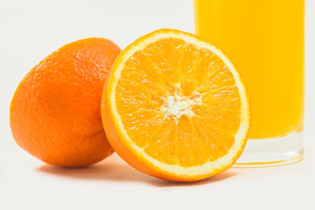 Rodajas de naranjas con un vaso de jugo de naranja sobre un fondo blanco.