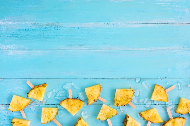 Rodajas de palitos de paleta de piña con hielo en color azul tablón de madera