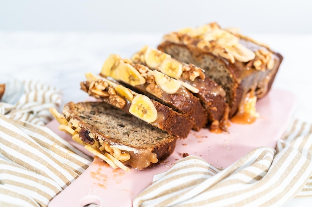 Rodajas de pan de nuez de plátano rociado con caramelo casero en una tabla de cortar rosa.