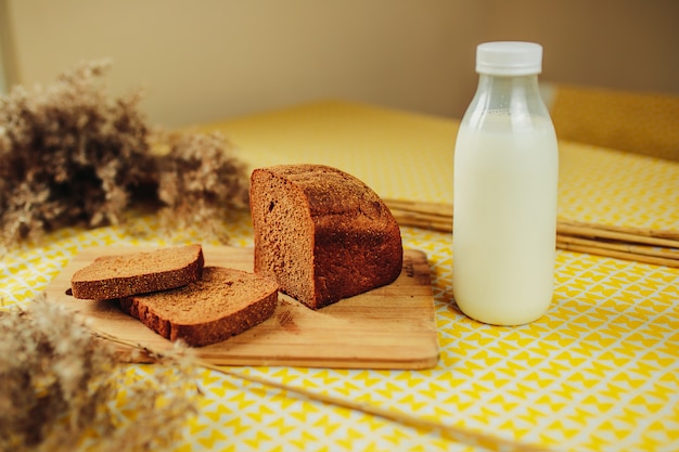 Rodajas de pan oscuro y botella de leche fresca en la mesa amarilla. Nutrición saludable, comida sana en la mesa. Botella de leche blanca y pan fresco.