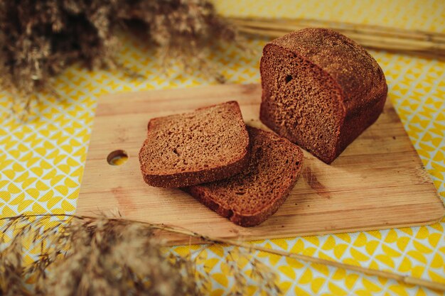 Rodajas de pan oscuro sobre tabla de madera. Nutrición saludable, comida sana en la mesa con flores secas.