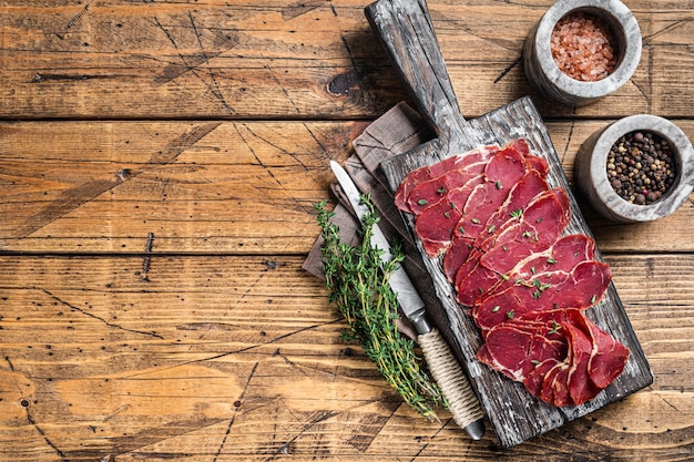 Rodajas de pastrami secas, carne de ternera con hierbas sobre tabla de madera. Fondo de madera. Vista superior. Copie el espacio.