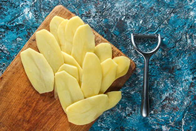 Rodajas de patatas en una plataforma de madera en la mesa de hormigón azul. Vista superior