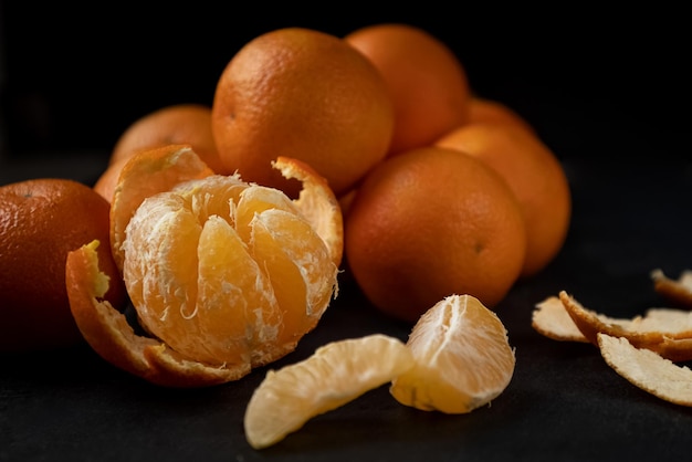 Rodajas peladas y mandarina medio pelada sobre fondo oscuro