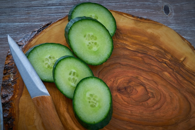 Rodajas de pepino y cuchillo de tablero de madera de olivo.