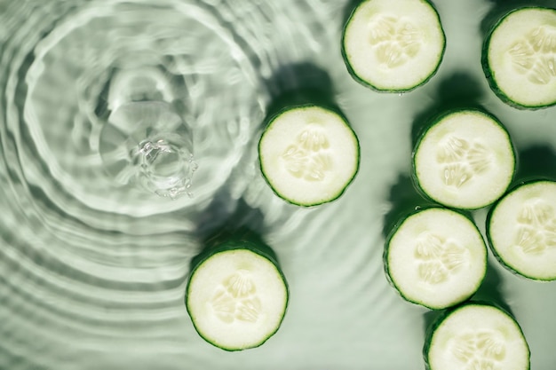 Rodajas de pepino se encuentran en la superficie de gel de agua verde fresco transparente ondulado con círculos de expansión de sombra de ondas fleck