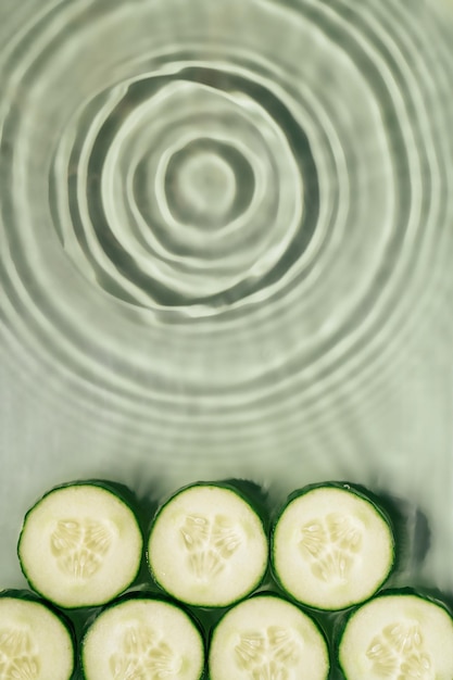 Rodajas de pepino se encuentran en la superficie de gel de agua verde fresco transparente ondulado con círculos de sombra de ondas fleck Vertical