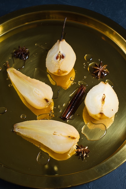 Rodajas de pera pochada en una bandeja de oro, cocida en vino blanco.