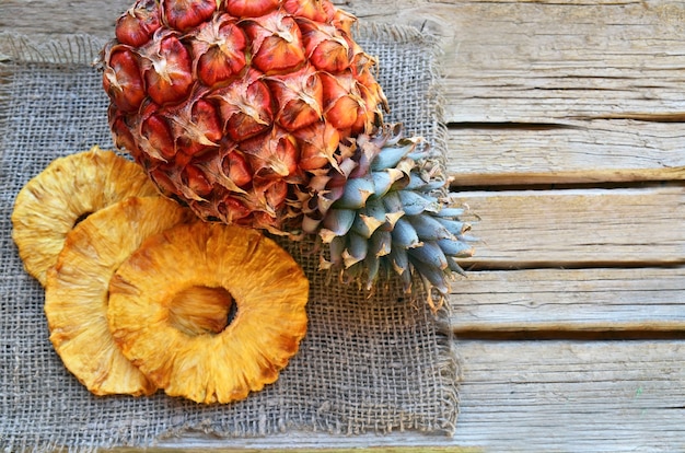 Rodajas de piña seca orgánica cruda y fruta fresca de piña madura en mesa rústica de madera.