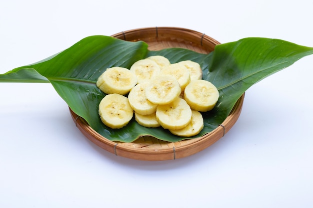 Rodajas de plátano en canasta de bambú sobre fondo blanco.