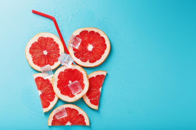 Rodajas de pomelo y cubitos de hielo con una pajita sobre un fondo azul en forma de cóctel. El concepto de la bebida de limonada es una composición refrescante de verano. Vista superior