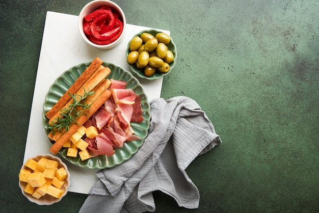 Rodajas de prosciutto o jamón palitos de grissini deliciosos con prosciutto queso romero aceitunas en plato verde en fondo oscuro aperitivos mesa con bocadillos italianos antipasto vista superior espacio de copia