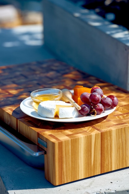 Rodajas de queso camembert y cheddar en un plato con uvas y miel. pícnic en la terraza