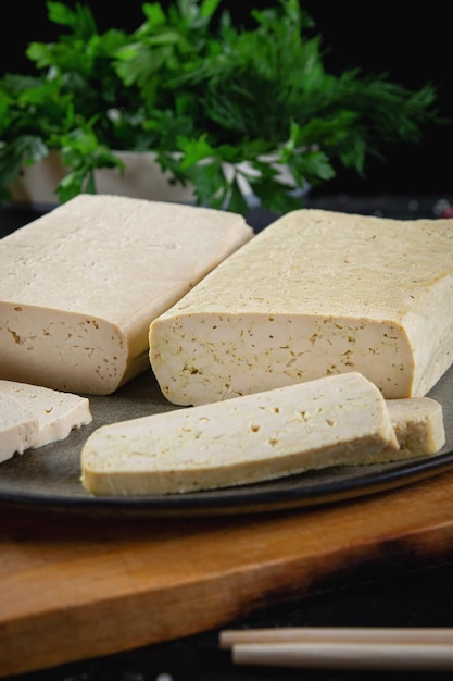 Rodajas de queso de soya tofu en una tabla para cortar con especias de albahaca y verduras