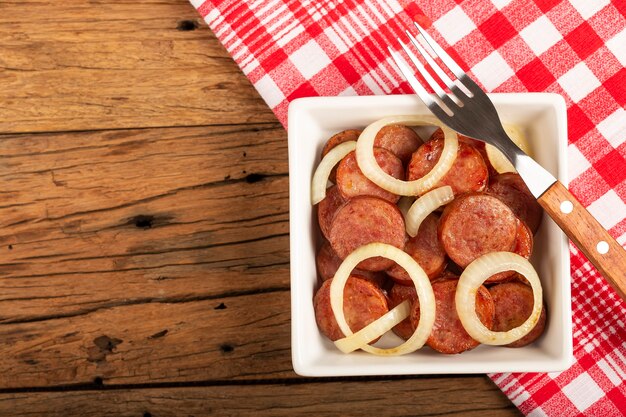 Rodajas de salchicha calabrese con cebolla sobre fondo de madera