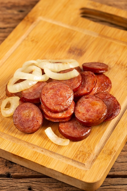 Rodajas de salchicha calabrese con cebolla sobre fondo de madera