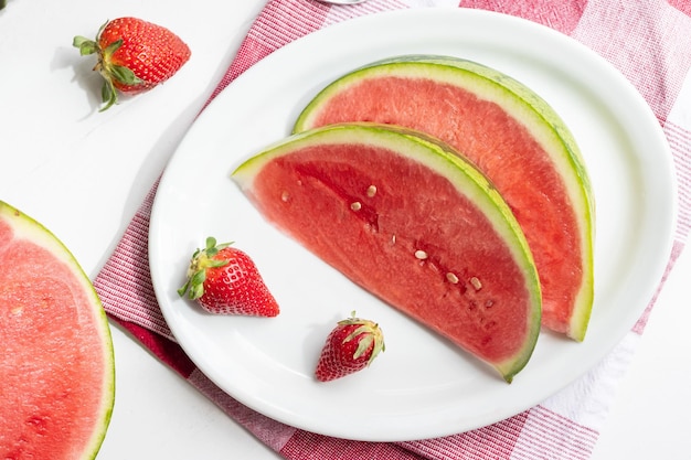 Rodajas de sandía de bayas de verano y fresas en un plato sobre una mesa blanca