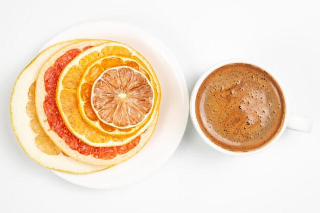 Rodajas secas de diversos cítricos y café negro en una taza blanca