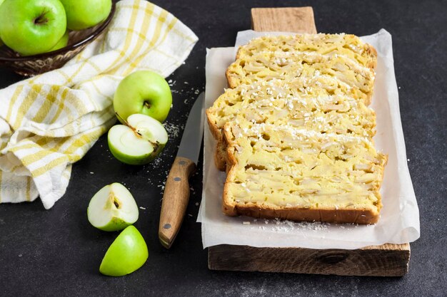 Rodajas de tarta de manzana y coco en la tabla de cortar de madera sobre fondo oscuro