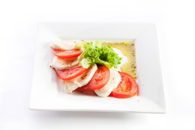 Rodajas de tomate y queso con lechuga sobre un fondo blanco.