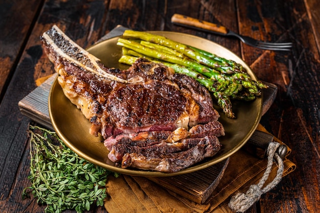 Rodajas de vaquero a la parrilla o ojo de costilla con espárragos asados de bistec de ternera en un plato Vista superior de fondo de madera