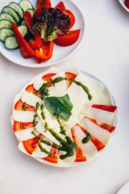 Rodajas de vegetales de pepino, tomate, pimiento y lechuga junto a rodajas de mozzarella y tomate con salsa pesto
