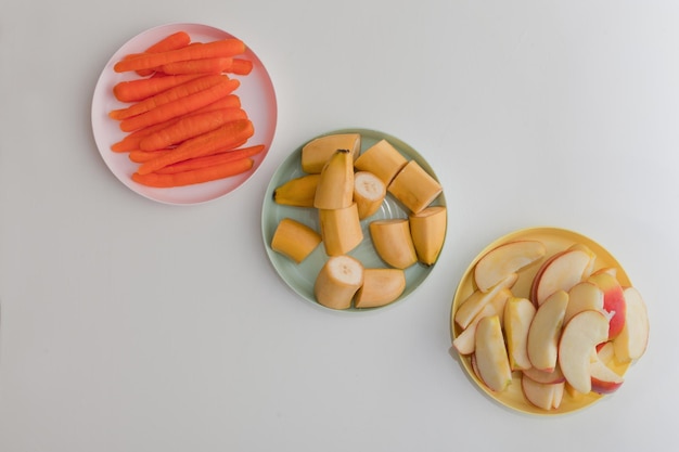 Rodajas de zanahoria, manzana y plátano en los platos, verduras y frutas frescas.