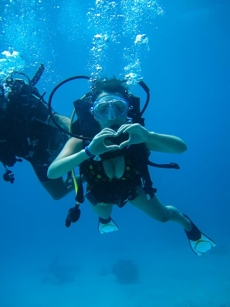 Rodaje submarino de una joven mujer buceando con escafandra y mostrando una señal de amor