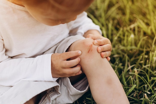 Foto una rodilla de niño tiene un rasguño y fluye en la sangre él sostiene su mano a la rodilla que le duele