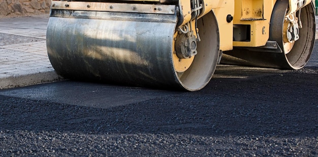 Rodillo de camino y máquina pavimentadora de asfalto en el sitio de construcción