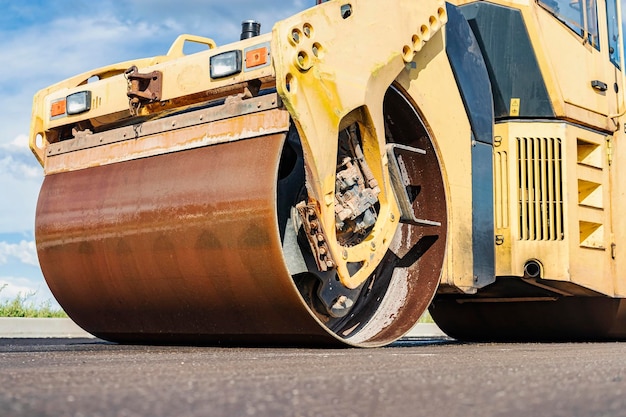 El rodillo compactador vibratorio coloca asfalto en una nueva carretera en construcción. Primer plano del trabajo de la maquinaria vial. Trabajos de construcción en la construcción de carreteras urbanas.