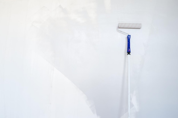 Foto el rodillo de esponja en un palo de madera vuelve a pintar la pared gris. renovación del hogar. copia espacio