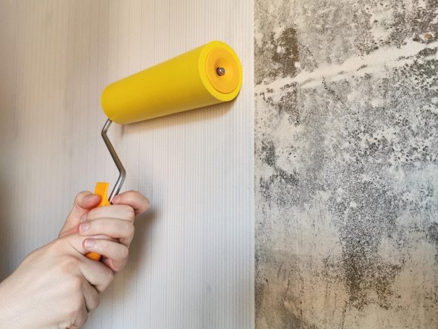 Rodillo de herramientas para alisar papel tapiz amarillo Rodillo de pintura con mango rojo y boquilla amarilla suave sobre un fondo claro Empapelado en el apartamento