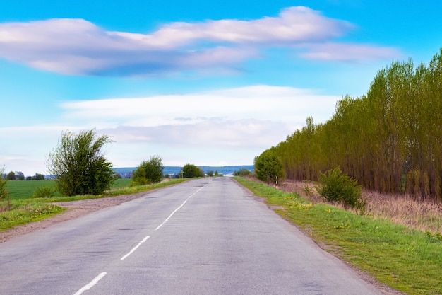 Rodovia com árvores em ambos os lados da estrada e céu alto com nuvens pitorescas.