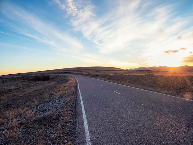 Rodovia de montanha vazia ao pôr do sol Estrada de asfalto e nuvens do céu ao pôr do sol Fundo da estrada