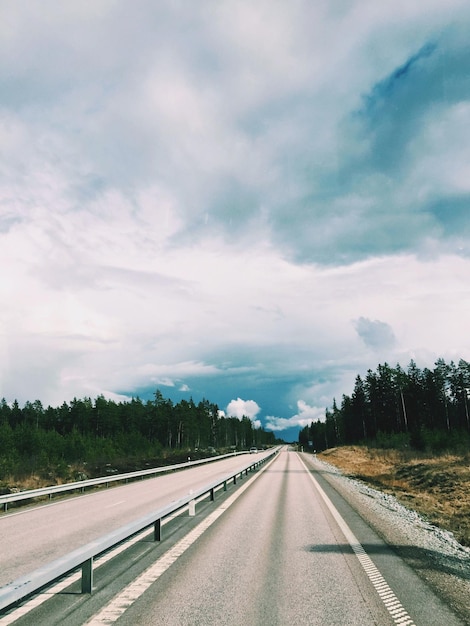 Rodovia em meio a árvores contra o céu nublado