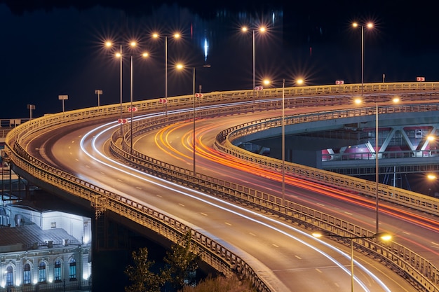 Rodovia nas luzes da noite. caminho rápido da luz do carro, trilhas e faixas na estrada da ponte de intercâmbio. listras pintadas à luz noturna