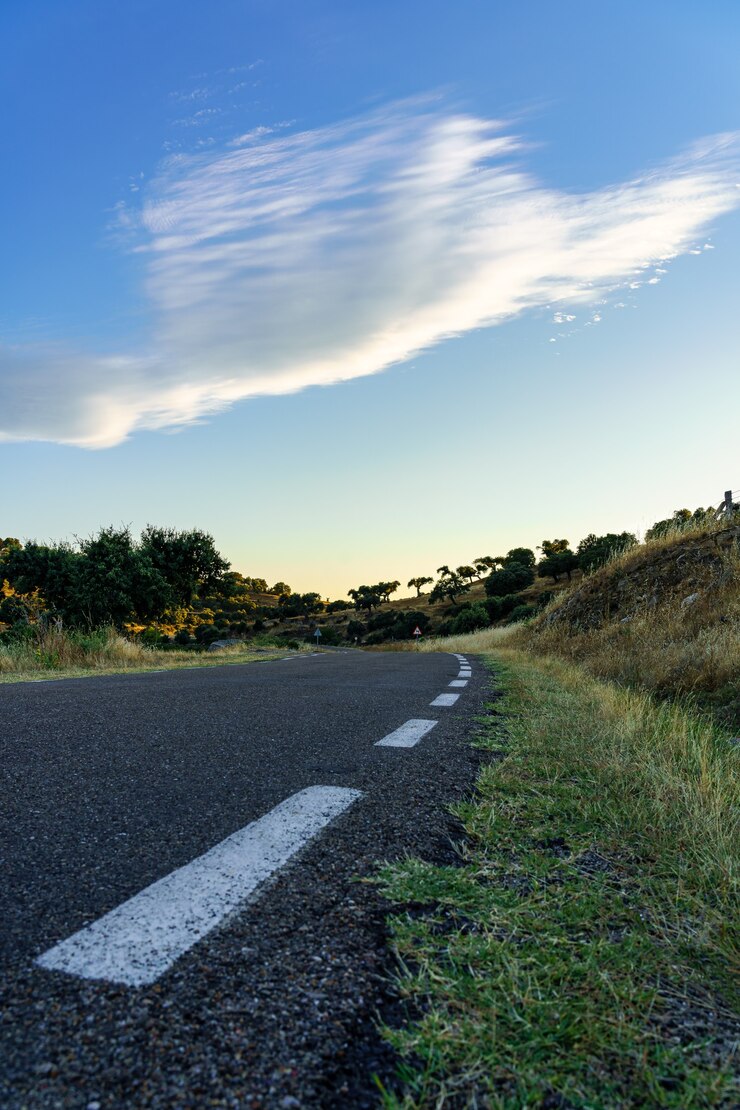 Rodovia para longe com céu azul e nuvem branca ao pôr do sol.