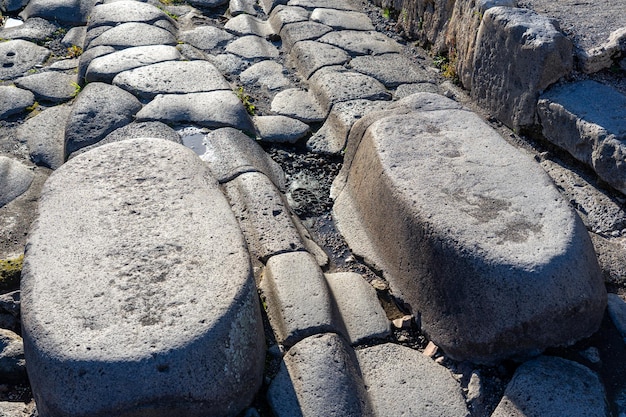 Römerstraße mit abgenutzten Steinen am Durchgang von Pferdekutschen im archäologischen Park von Pompeji