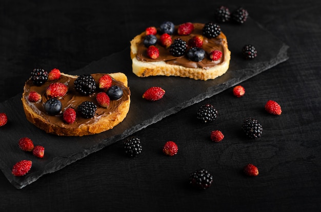 Rösten Sie mit Schokoladennussbutter mit frischen wilden Beeren auf dunklem Hintergrund