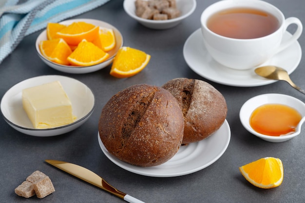 Roggenbrötchen und Frühstücksbutter mit Tee und Orange