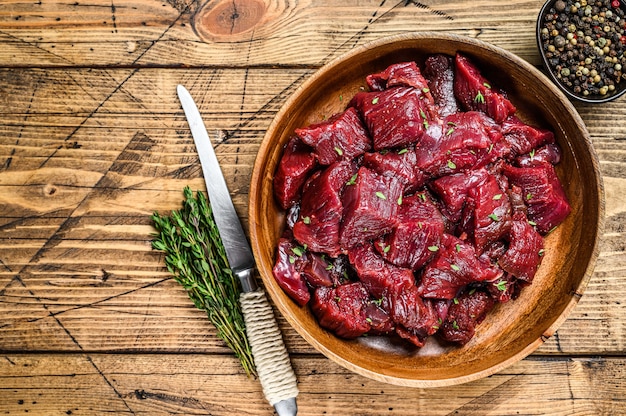 Roh geschnittenes Wildfleisch für ein Gulasch in einer Holzplatte. Hölzerner Hintergrund. Ansicht von oben. Platz kopieren.