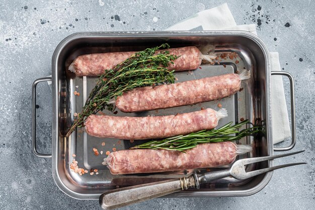 Rohe Bratwurst-Schweinefleischwürste in einem Küchentablett. Grauer Hintergrund. Ansicht von oben.