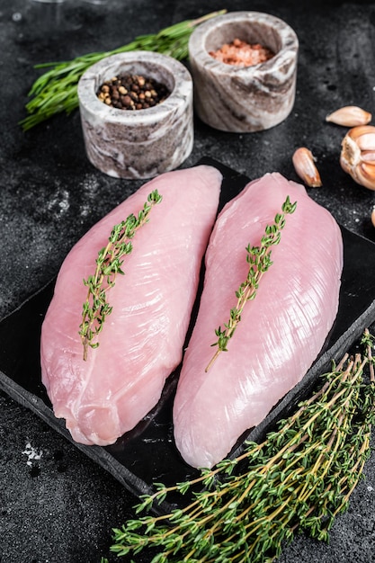 Rohe Brustfiletsteaks der Türkei auf Marmorplatte mit Kräutern Schwarzer Hintergrund Ansicht von oben