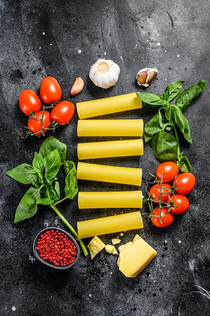 Rohe Cannelloni-Nudeln und Gemüse auf einem schwarzen Tisch