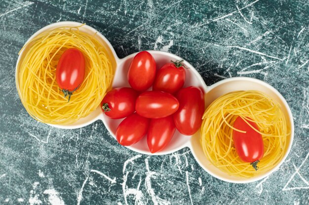 Rohe Capellini-Nudeln und Tomaten in einer Schüssel auf der blauen Oberfläche