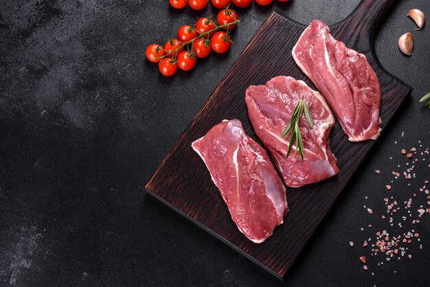 Rohe Entenbrust mit Kräutern und Gewürzen auf einem dunklen Tisch. Rohes Fleisch zum Backen vorbereitet